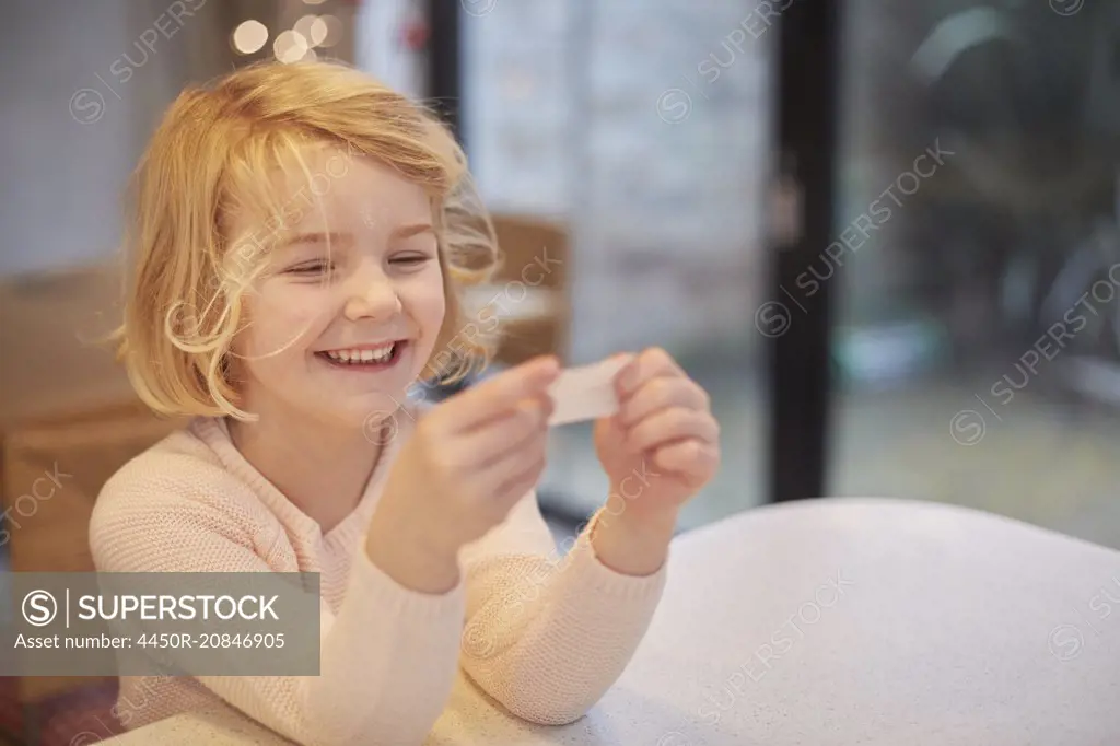 A young girl laughing and looking at a small piece of paper, a joke from a Christmas cracker.