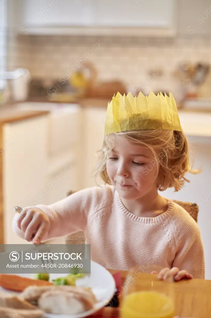 A young girl wearing a party hat, sitting at a table having a meal.