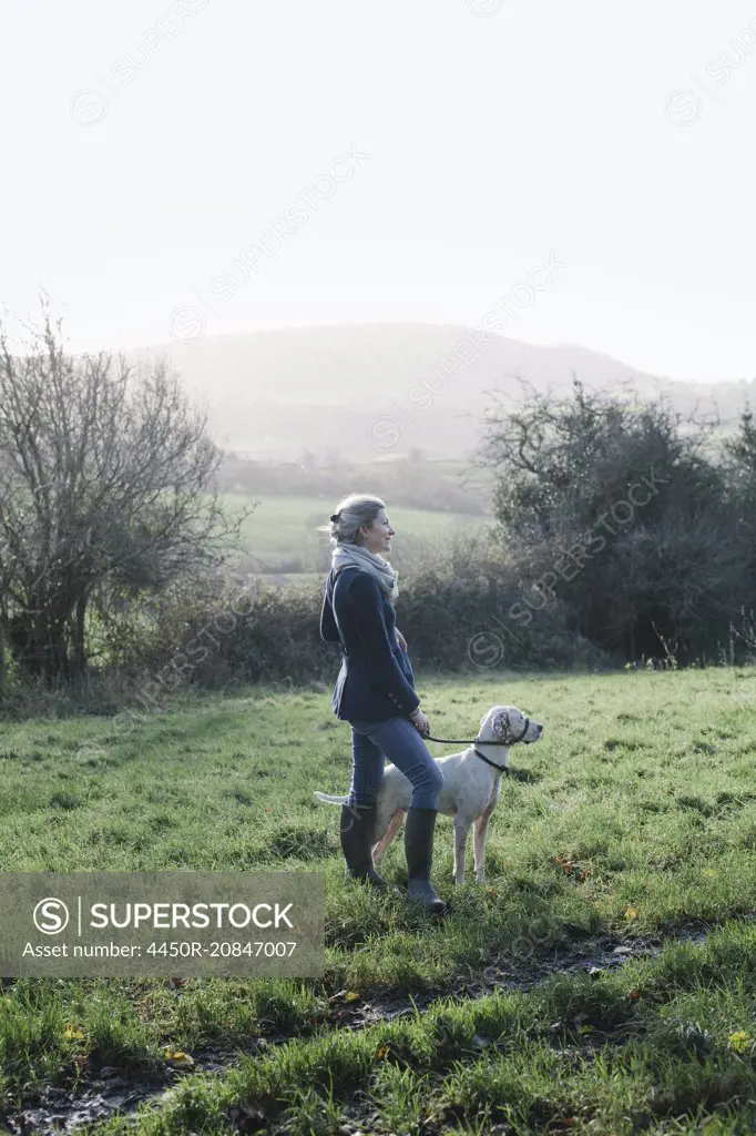 A woman walking with a dog on high ground overlooking the countryside.