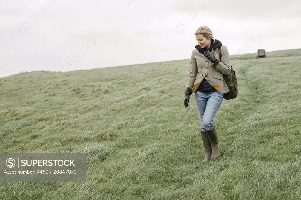 A woman in warm coat and gloves walking across open country, grassland and moors.