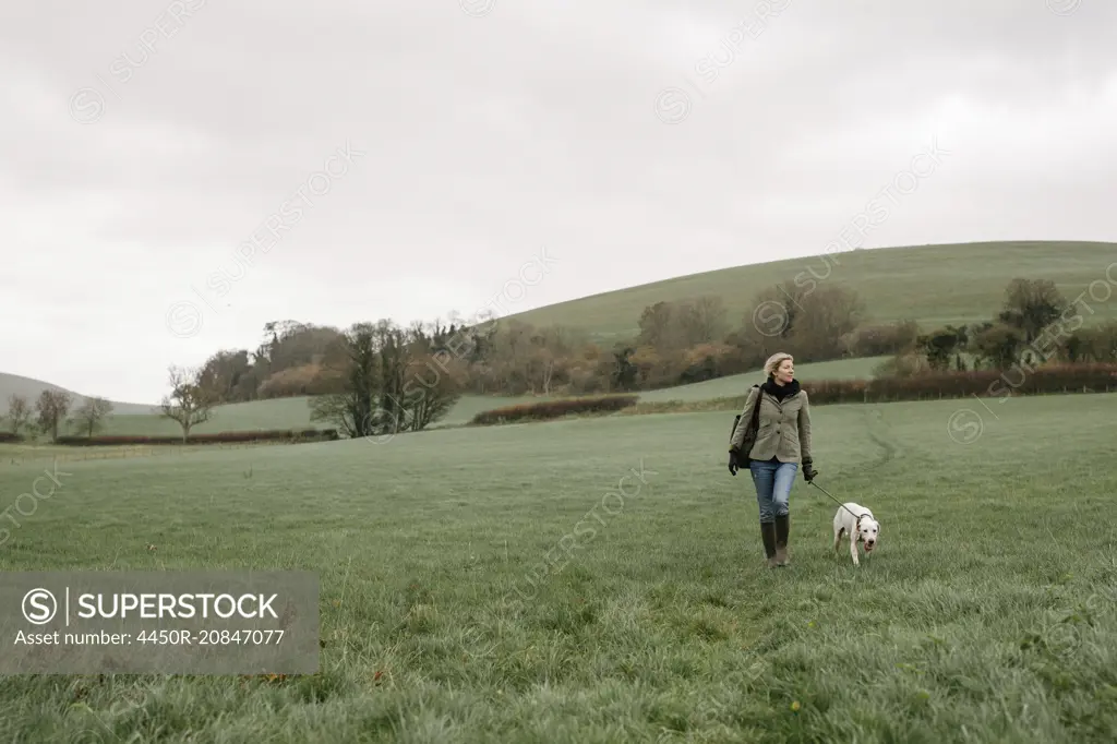 A woman walking with a dog across a grass field.