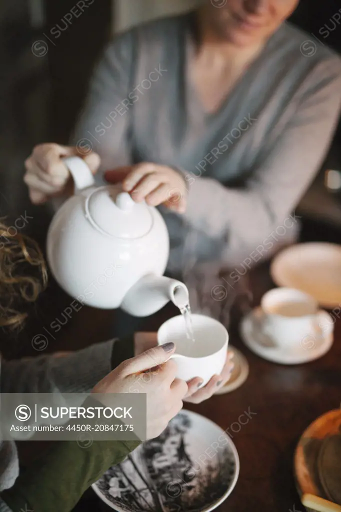A woman pouring tea from a teapot into a cup for a companion.