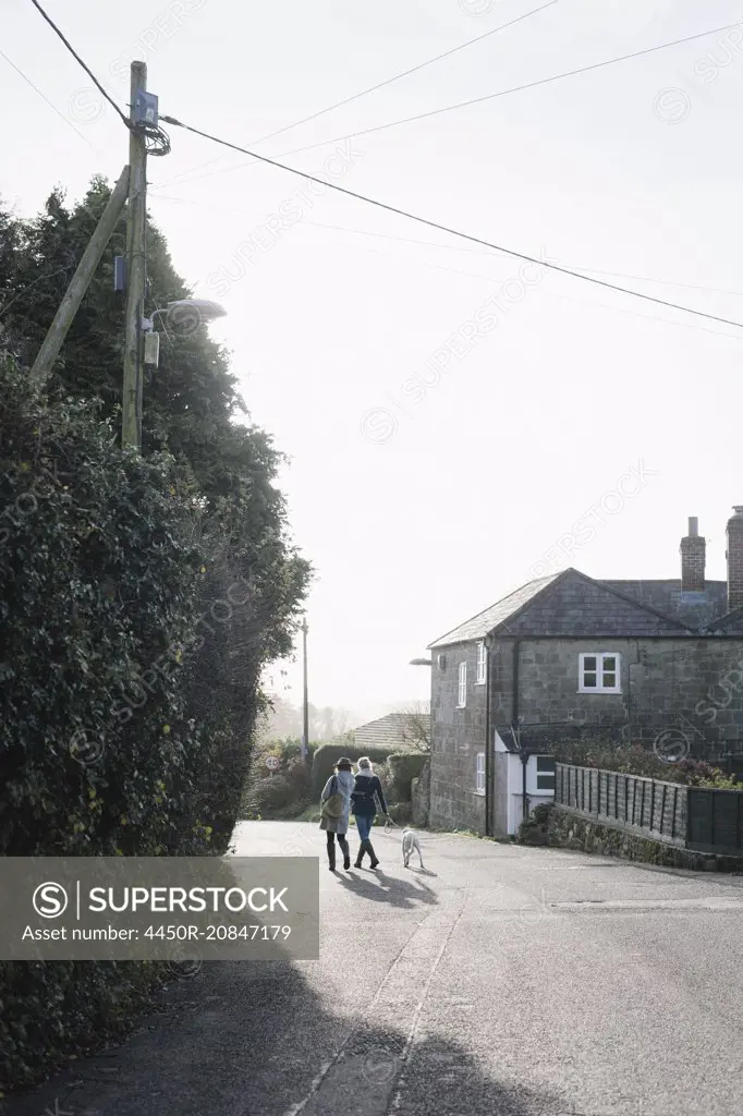 Two women walking along a village street with a dog on a lead.