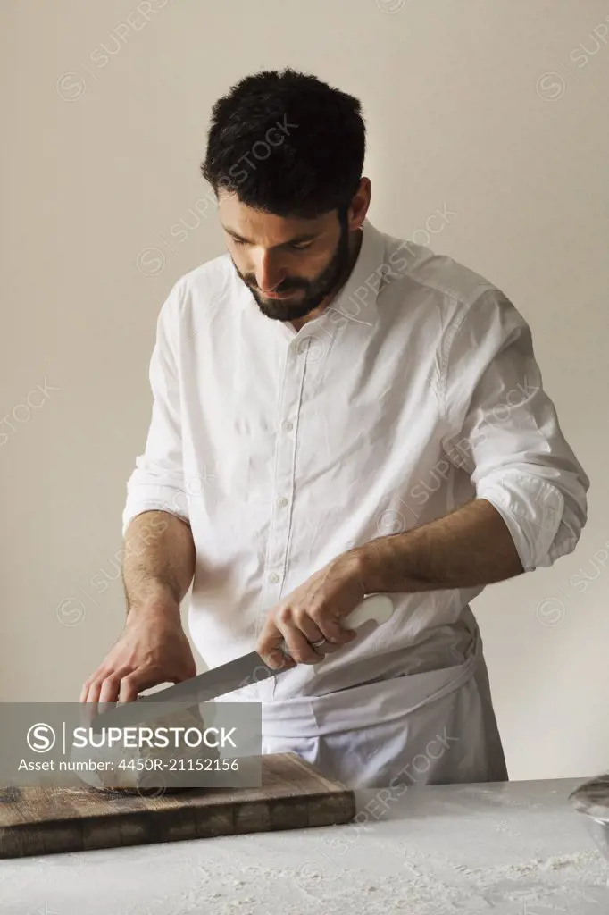 Baker slicing a freshly baked loaf of bread with a bread knife.