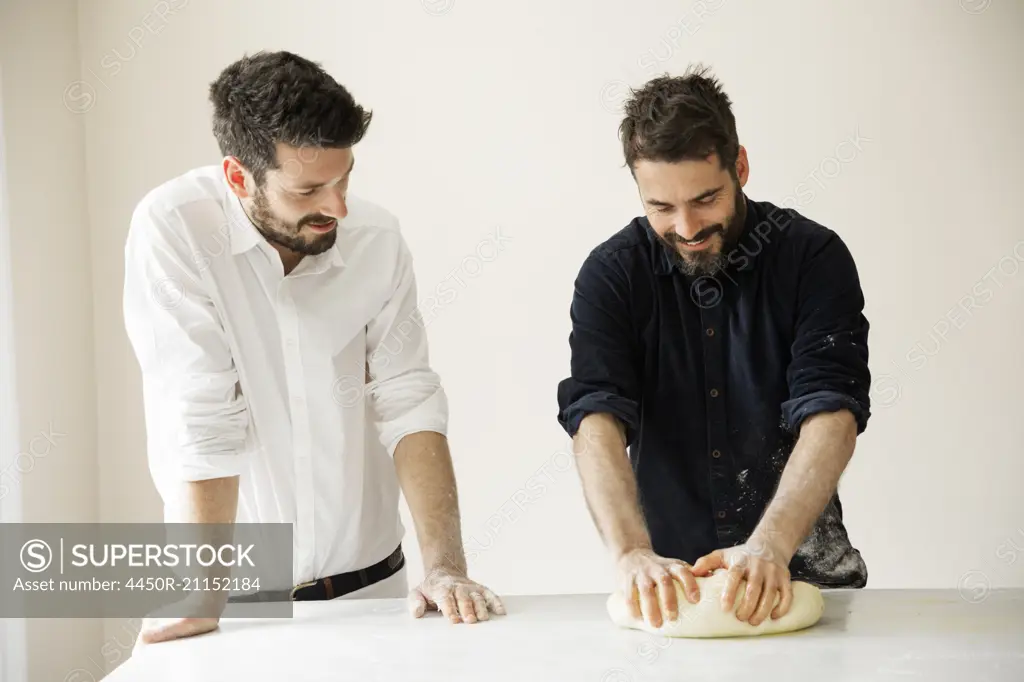 Two bakers standing at a table, kneading bread dough.