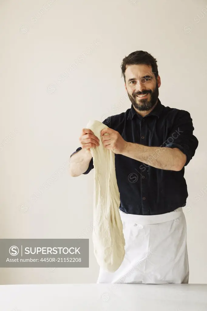 Smiling baker holding up a large portion of bread dough.