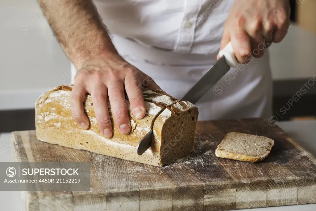 Close up of a baker slicing a freshly baked loaf of bread with a bread knife.