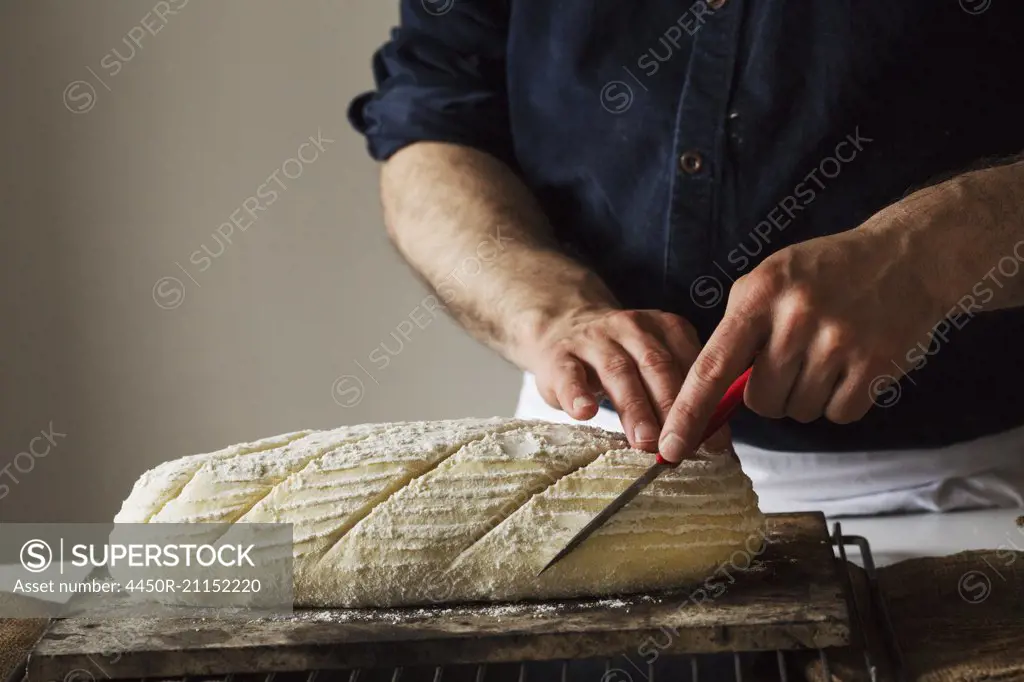 Close up of a baker slicing a freshly baked loaf of bread with a bread knife.