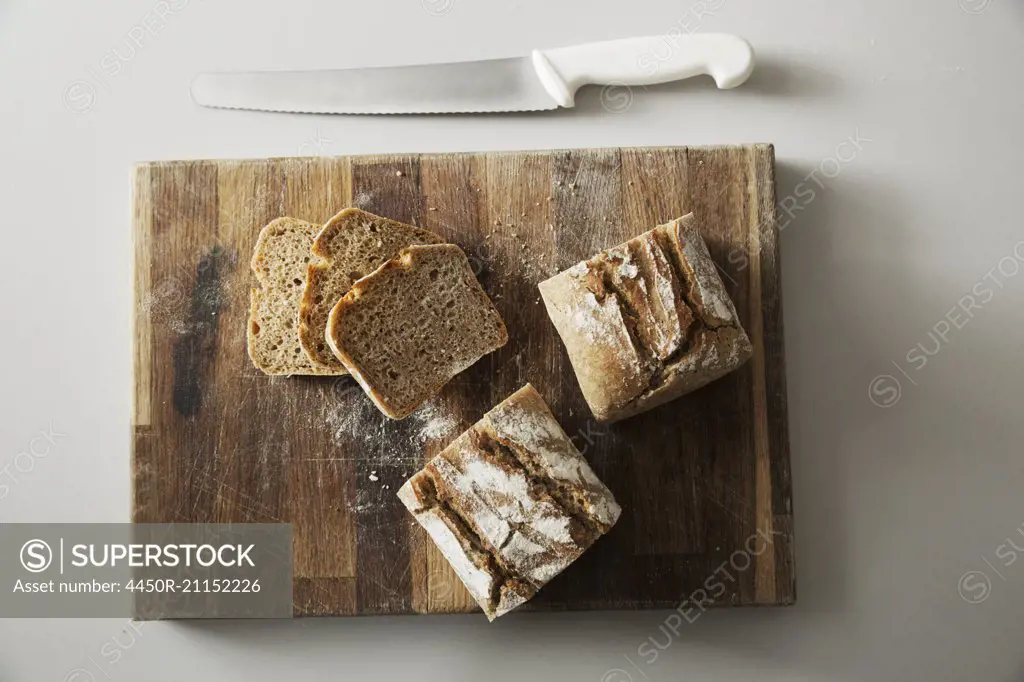 High angle view of a freshly baked loaf of bread and slices on a wooden chopping board, a bread knife.