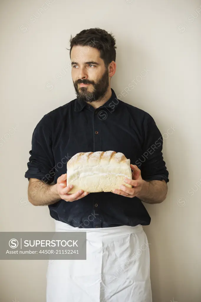 Baker holding a loaf of freshly baked white bread.