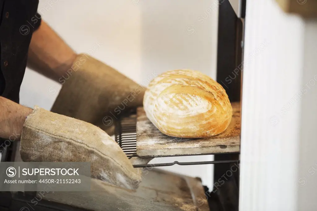 Close up of a baker taking a freshly baked loaf bread out of an oven.