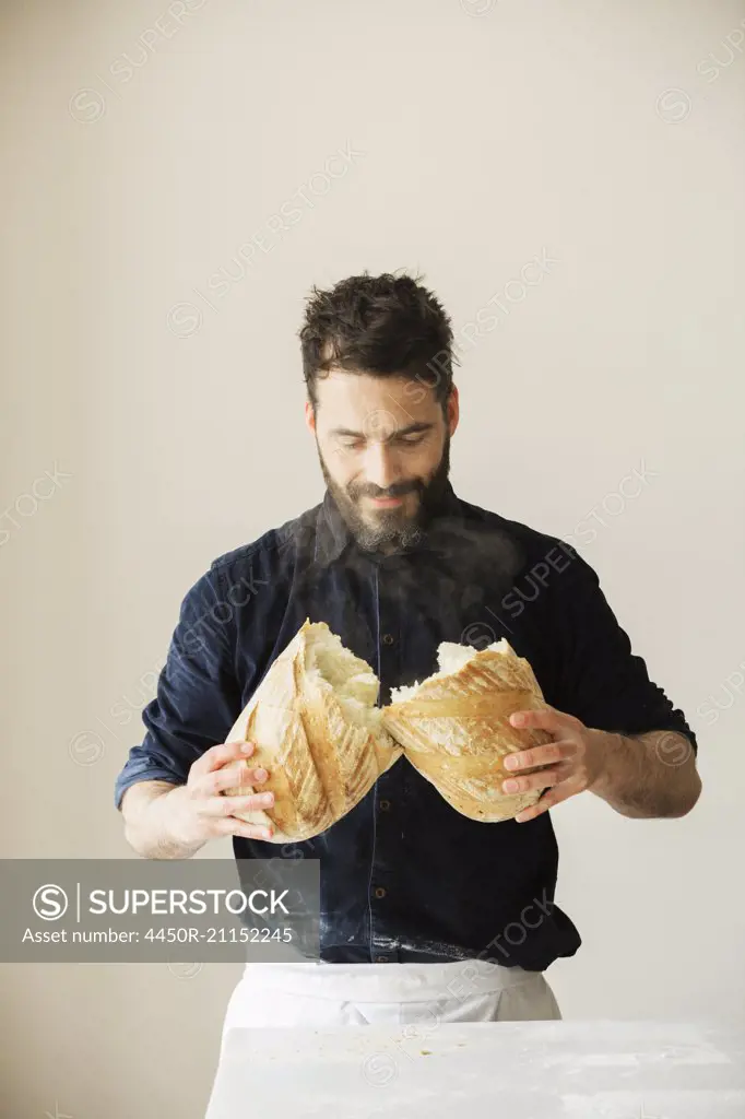Baker holding two freshly baked loaves of bread.