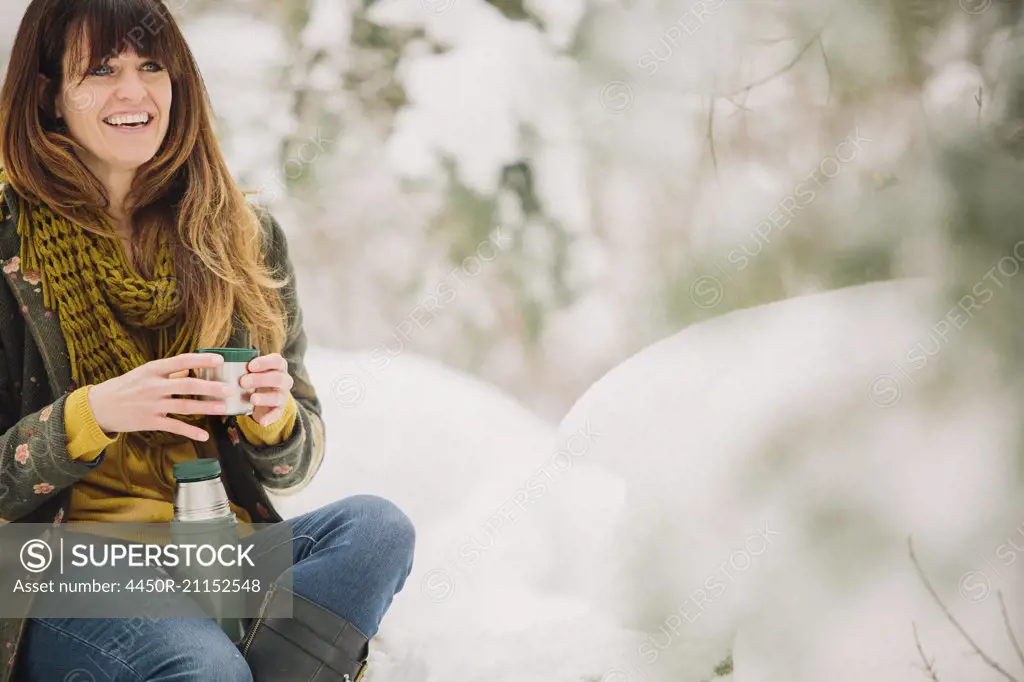 A woman in snow in winter, having a warm cup of coffee.