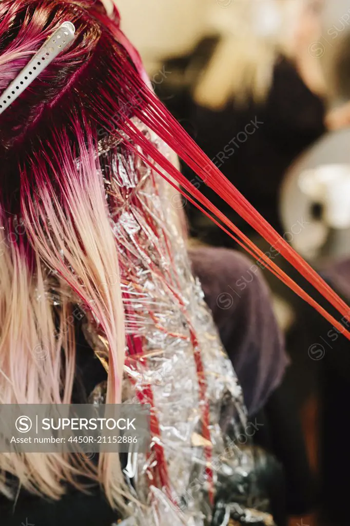 A hair colourist applying pink hair colour to a client's long blonde hair.