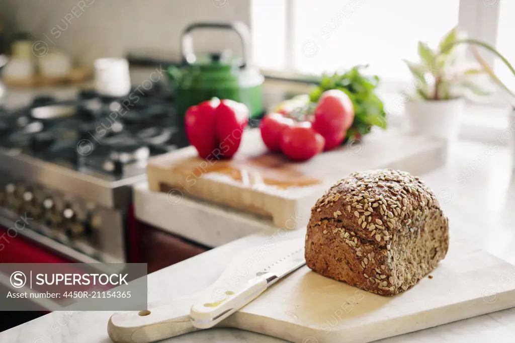 A fresh loaf of baked brown bread on a board with a breadknife.