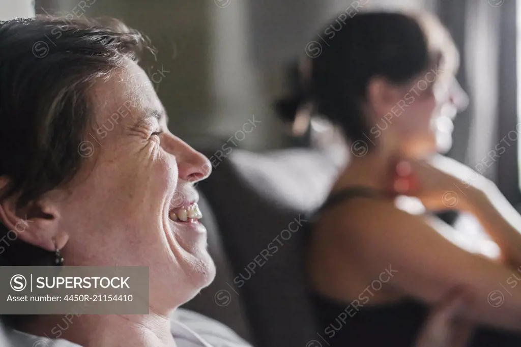 Two women in profile sitting at home, laughing.