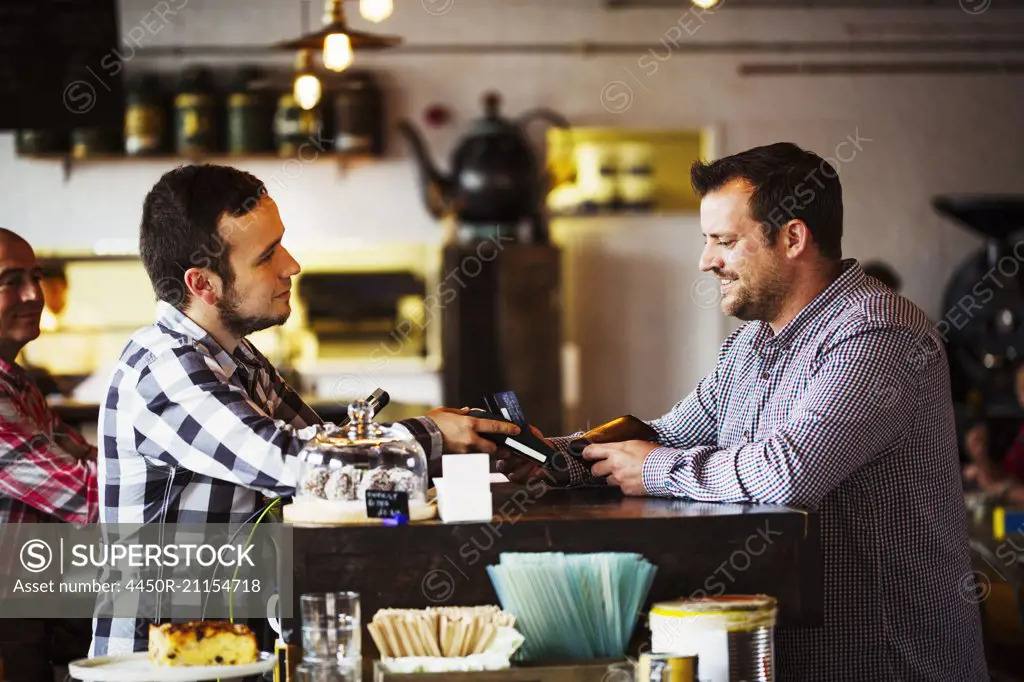 Specialist coffee shop. Two men, a barista and a client talking over the coffee shop counter.