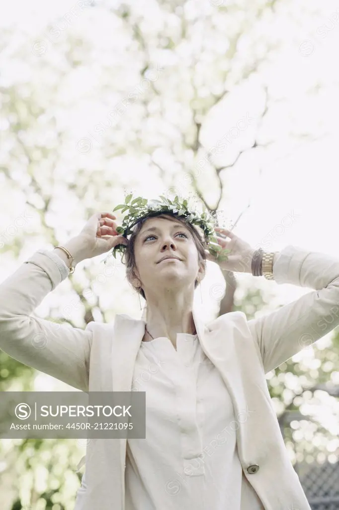 Woman standing in a garden, putting a flower wreath in her hair.