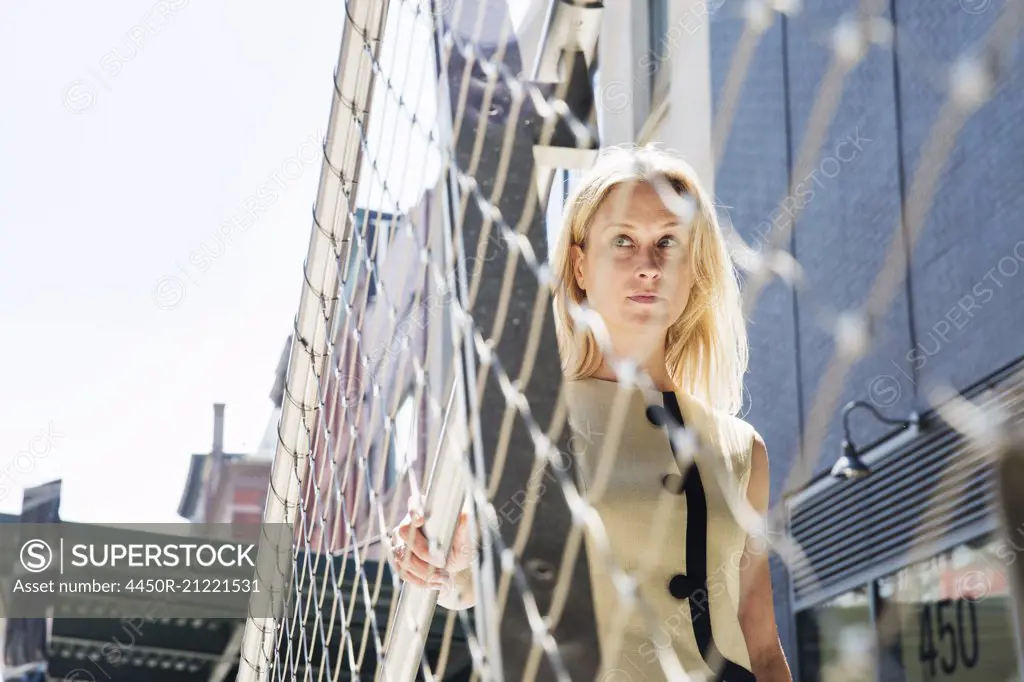Businesswoman standing at a metal wire fence in New York.