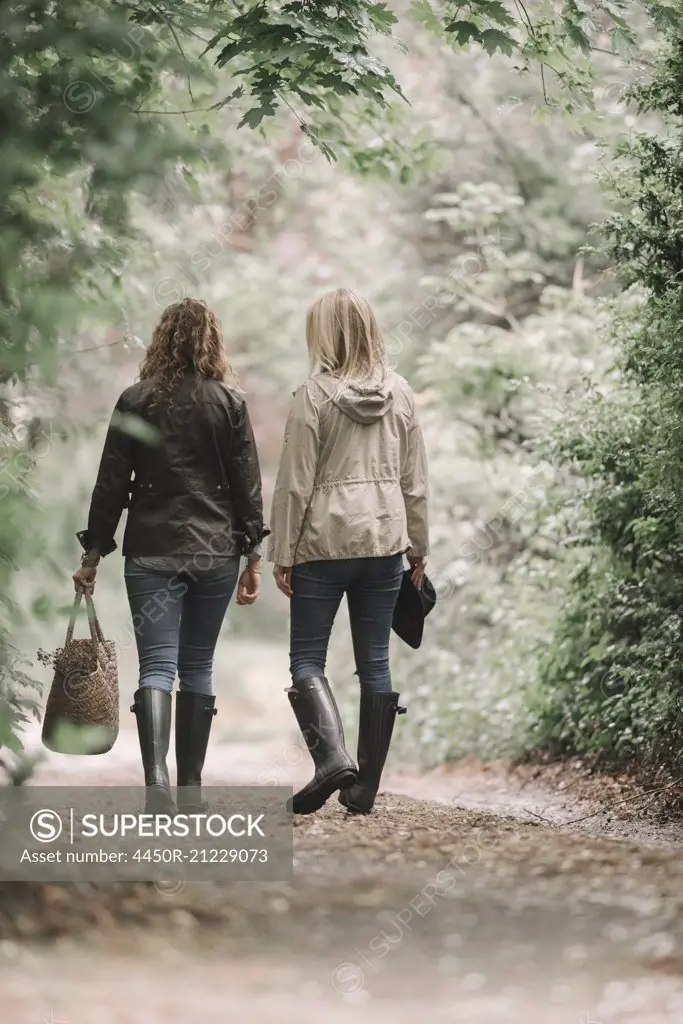 Two women walking in coats and boots along a country path with a basket.