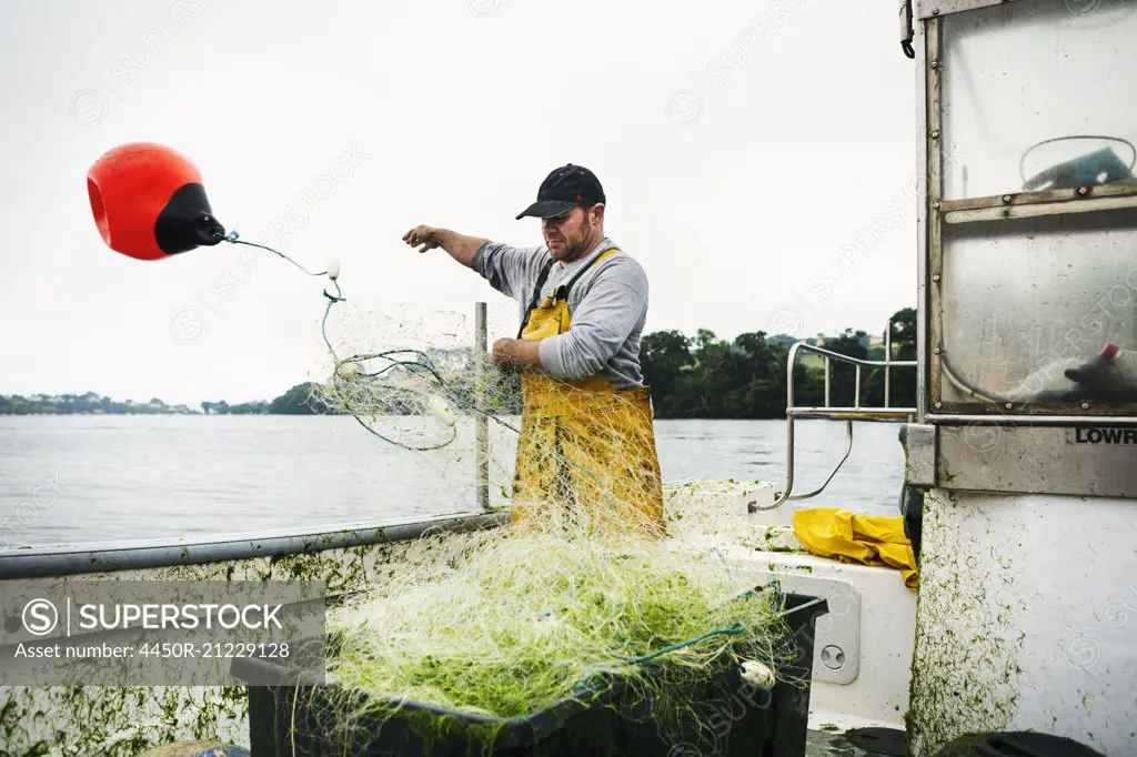 A fisherman standing on a boat throwing the floats out to spread the net over the water.