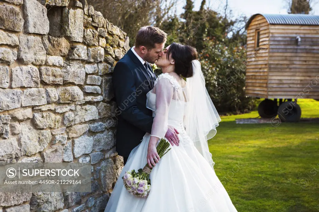 A bride and groom kissing on their wedding day standing in a garden.