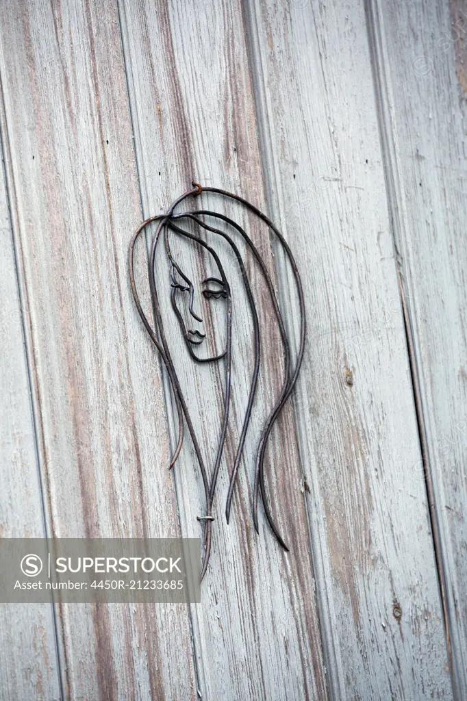 A wire metal sculture of a woman's face on a wood plank wall.