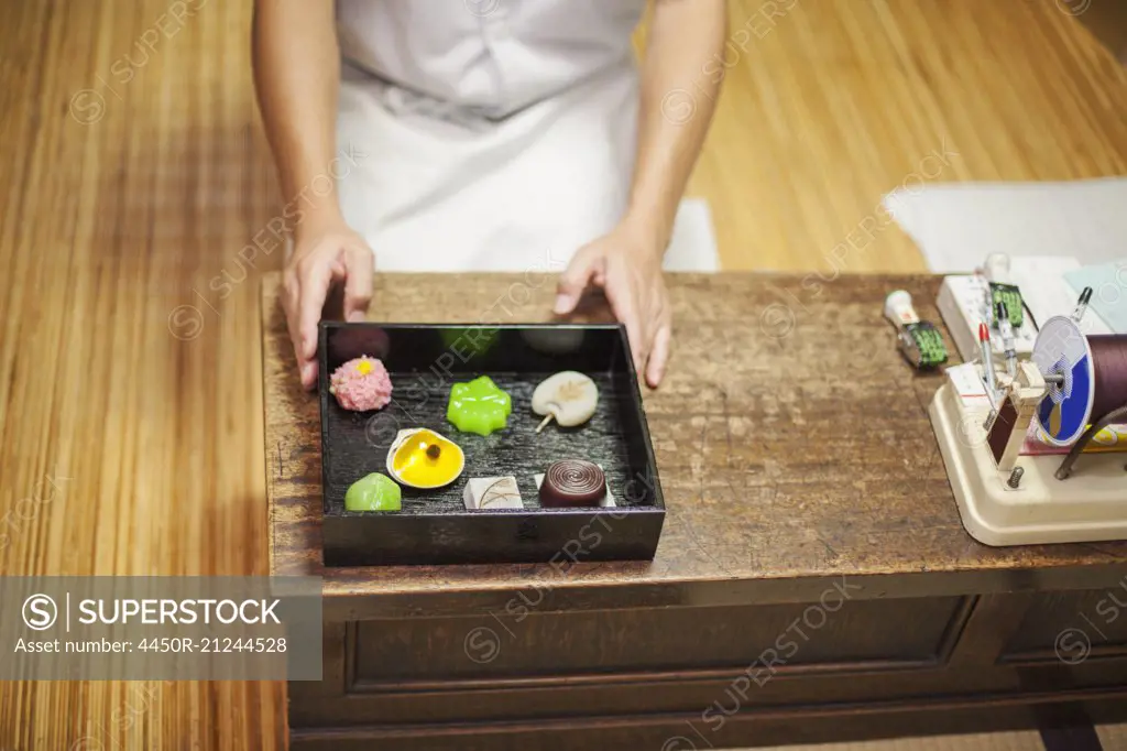 A small artisan producer of specialist treats, sweets called wagashi. A chef presenting a tray of selected wagashi of different shapes and flavours.