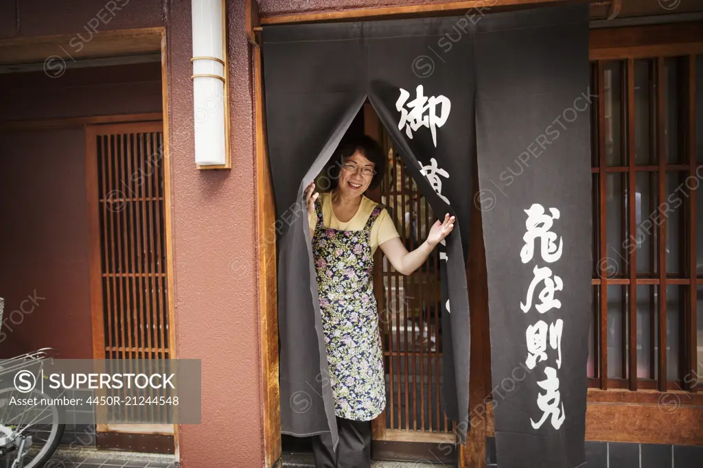 A small artisan producer of specialist treats, sweets called wagashi. A woman at the doorway of the shop.