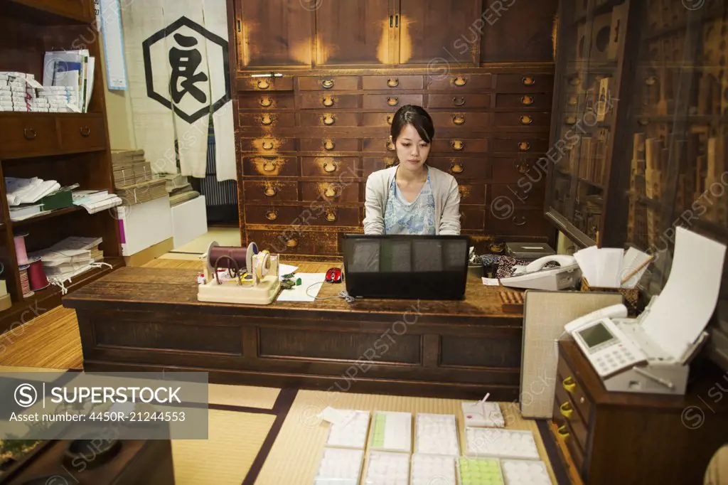 A traditional wagashi sweet shop. A woman working at a desk using a laptop and phone.