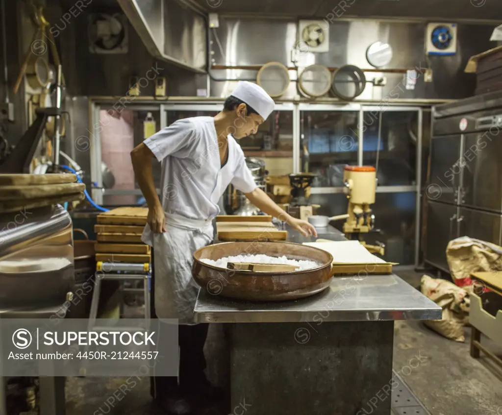 A small artisan producer of wagashi. A man mixing a large bowl of ingredients and pressing the mixed dough into moulds in a commercial kitchen.