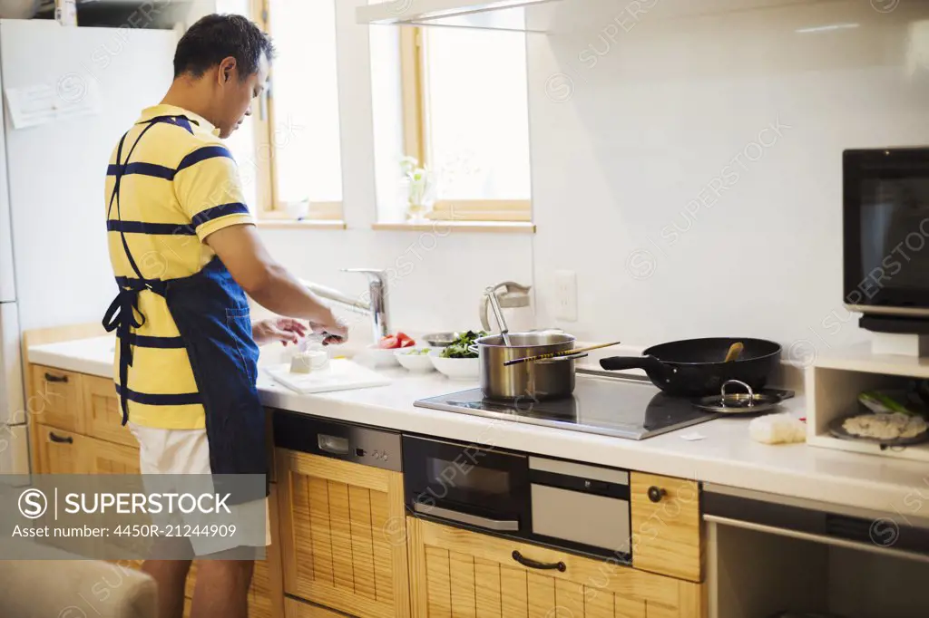 Family home. A man in a blue apron preparing a meal with his son.