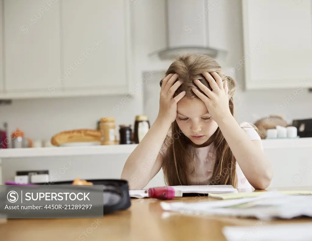 A girl sitting at a table with her hands on her head, looking at her homework.