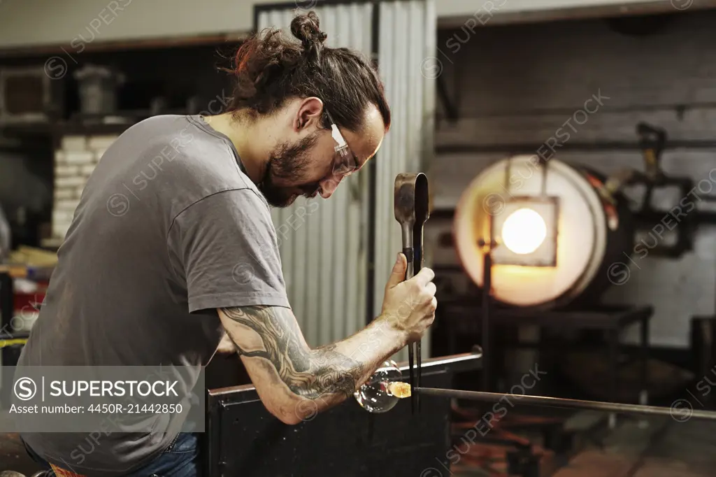 A glassblower with pliers working on a piece of glass.