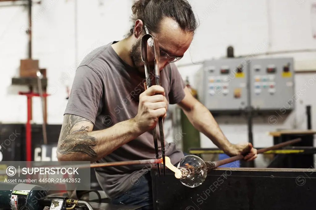 A glassblower with pliers working on a piece of glass.