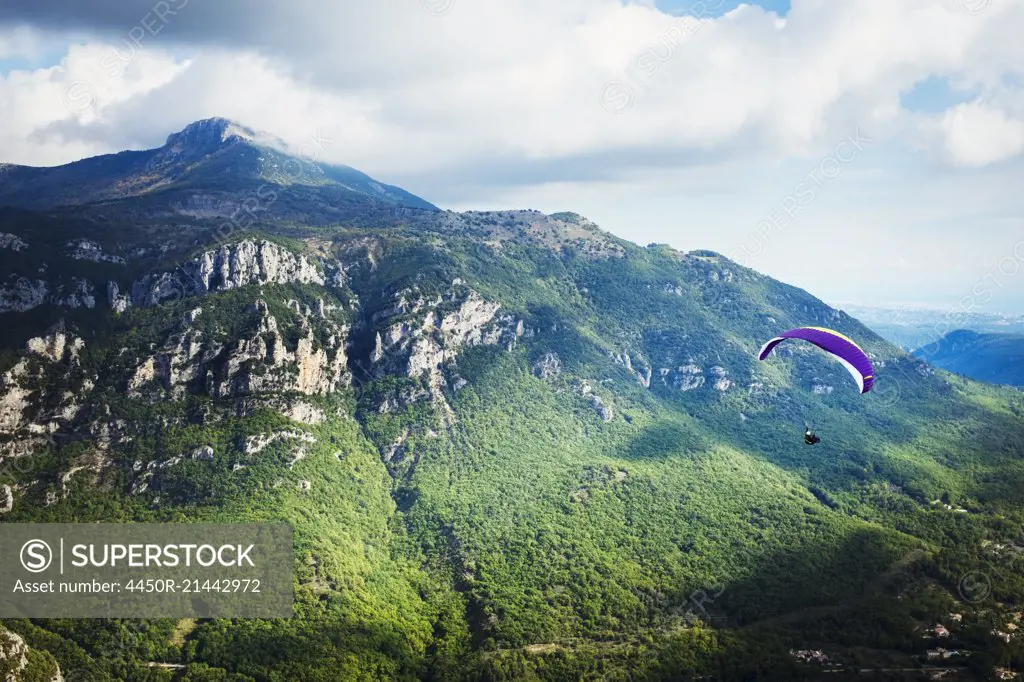 A paraglider in flight over a valley in the mountains.