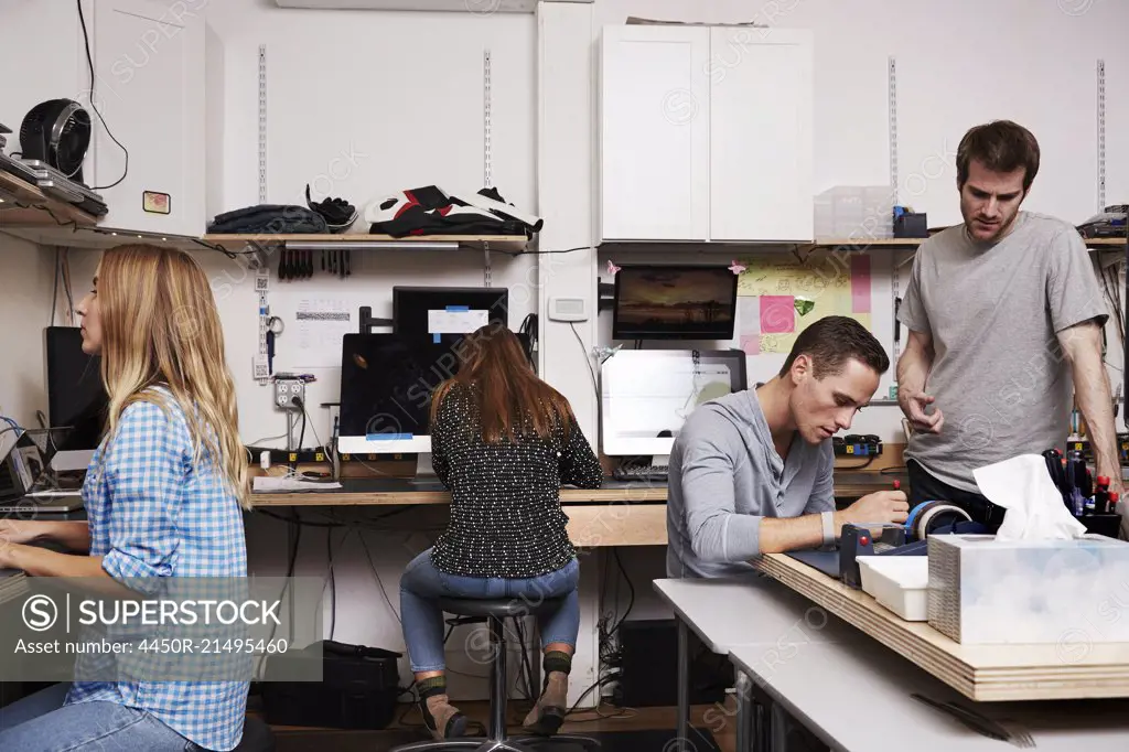 Two women and two men in a technology repair shop or lab, working on computers.