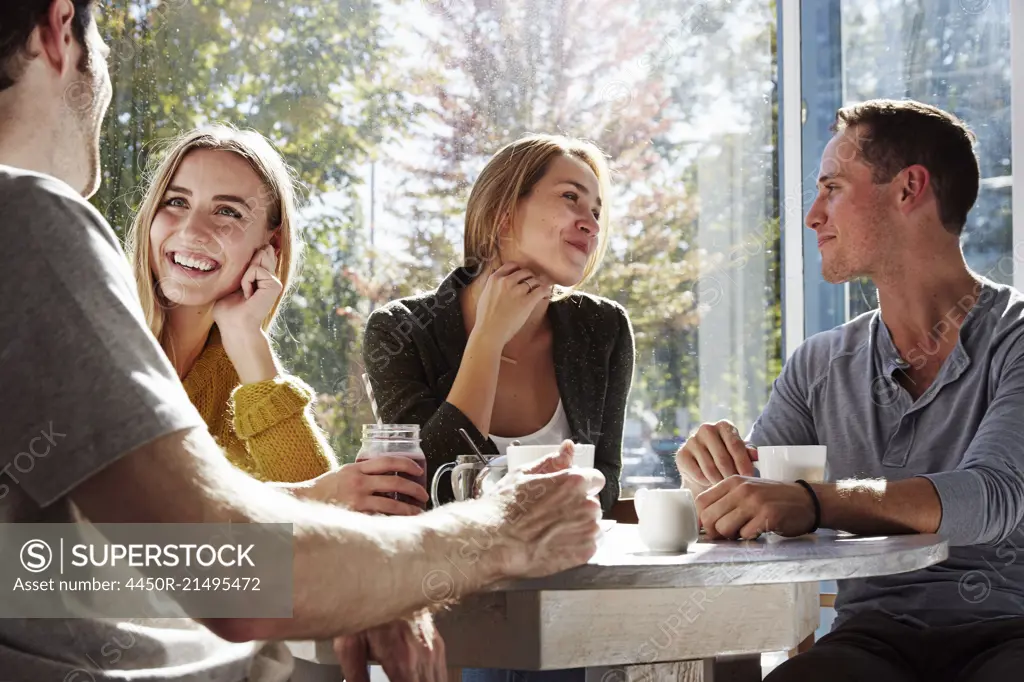 Four people sitting at a table talking, with mugs and jars of smoothies.