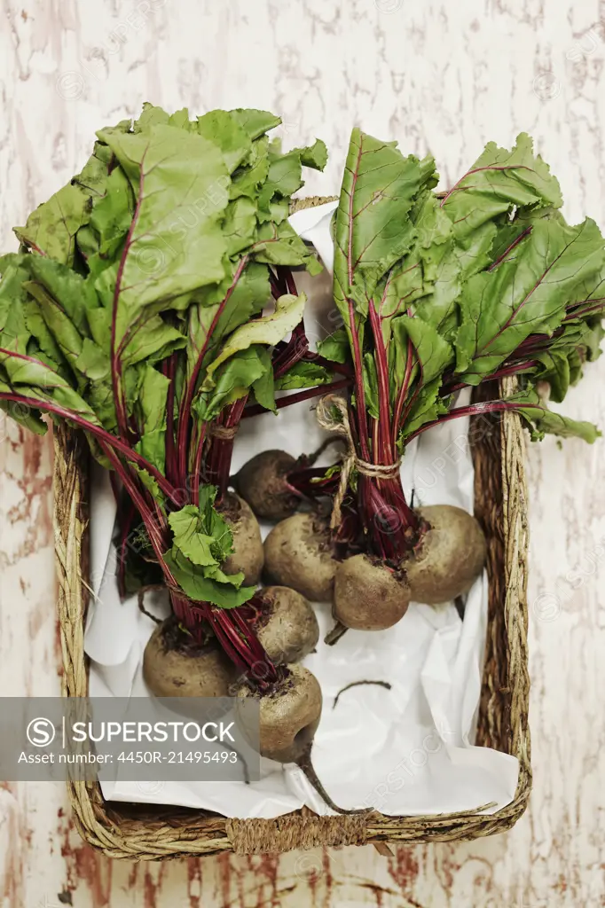 A shot of bundles of beets in a basket on a wooden surface, seen from above.