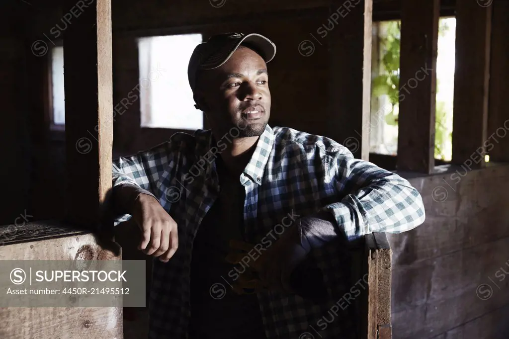 A young man in working clothes standing inside a wooden farm building.