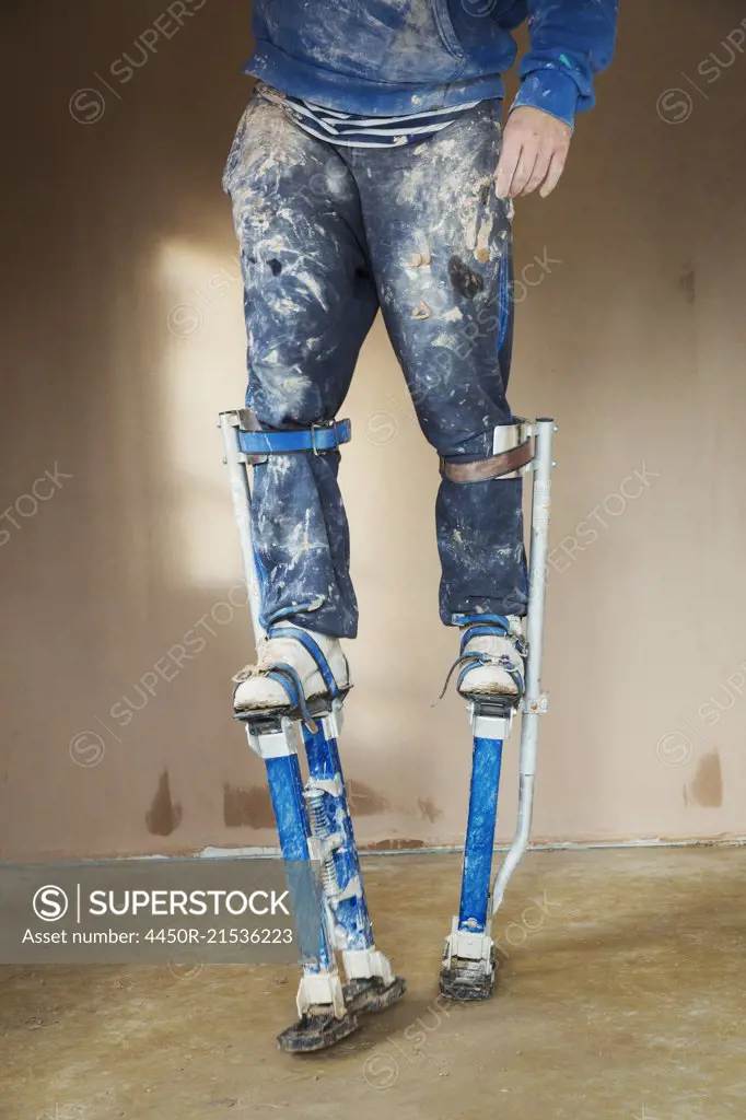 A plasterer wearing stilts working on the walls of a house under construction.