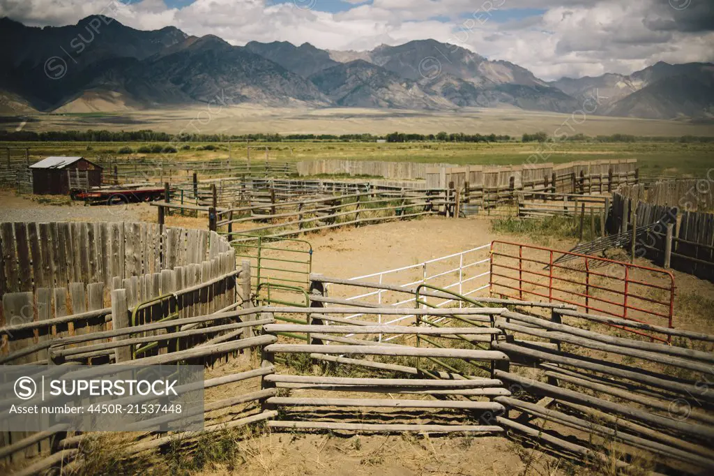 Empty cattle pens in a rural landscape with a mountain range behind.