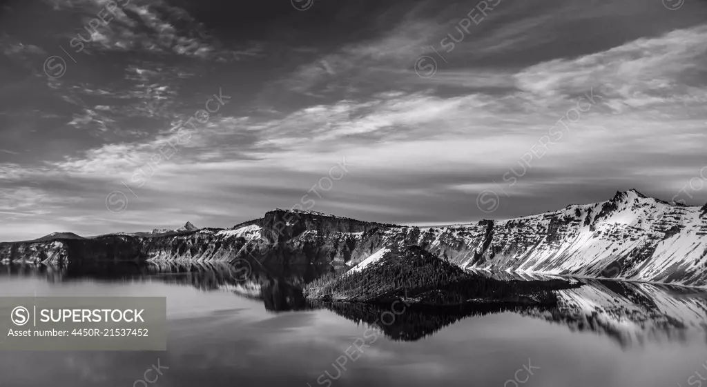 A lake reflecting a hilly landscape under a cloudy sky.
