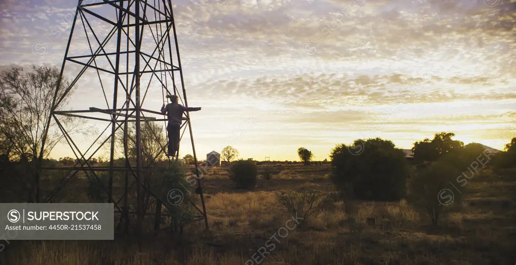 A person climbing a pylon in a rural landscape.