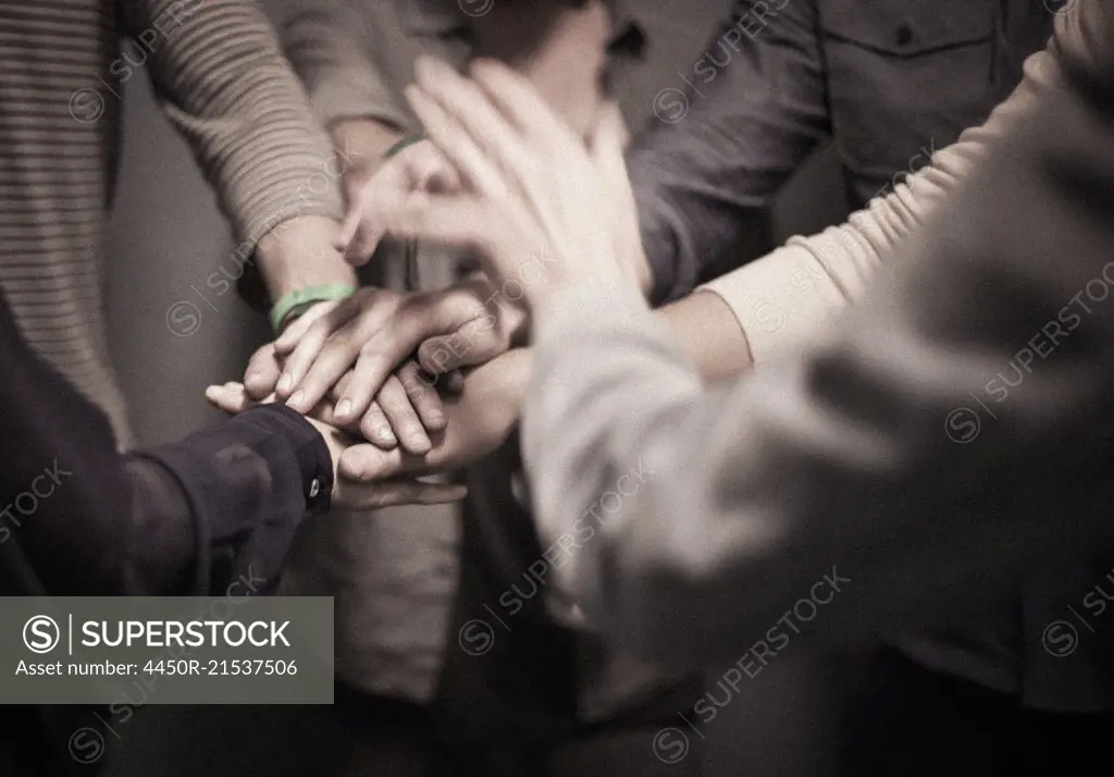 People standing with their hands layered in a team gesture.