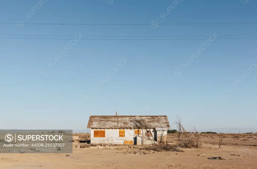 A boarded-up wooden house in an arid landscape against a blue sky.