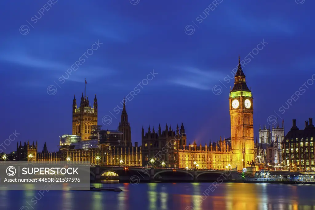 London landmarks, Big Ben and the Houses of Parliament lit up at night, with the river Thames in the foreground.