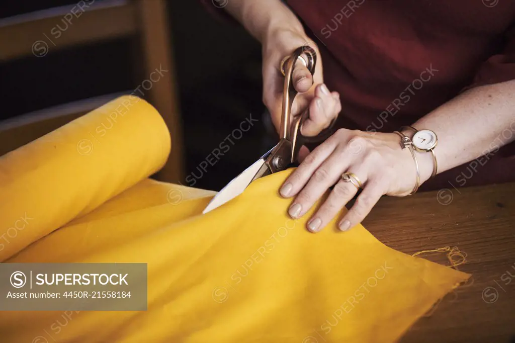 A woman seated at a table using dressmaing scissors to cut yellow material.