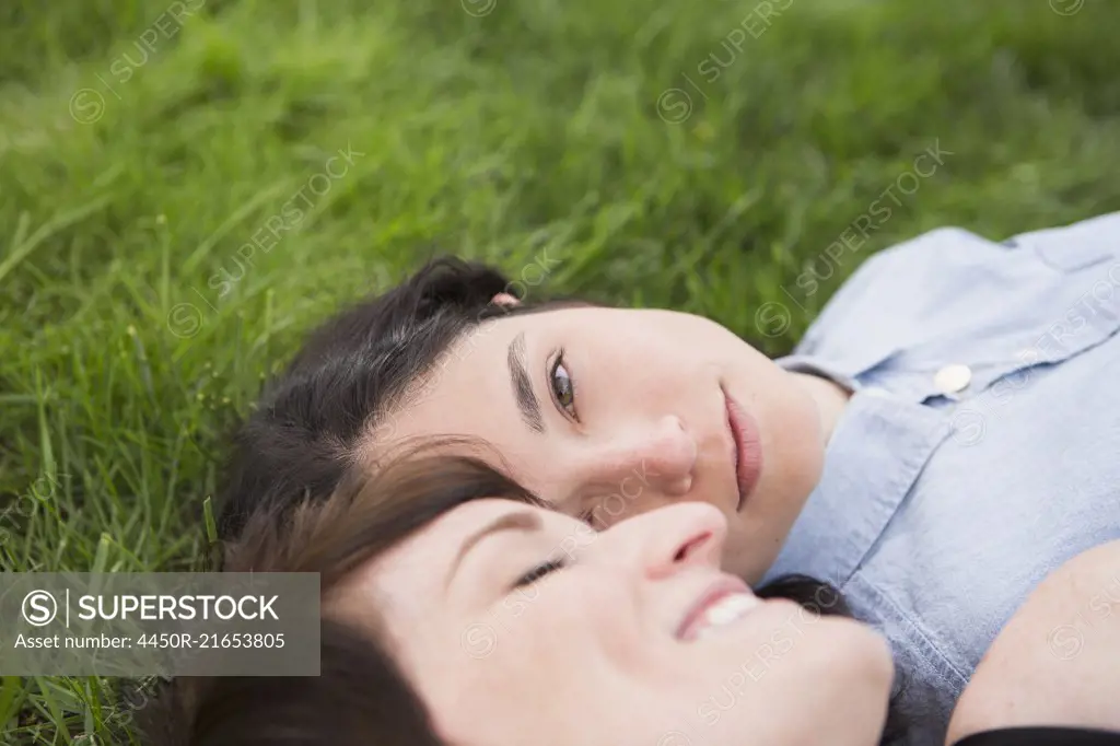 A same sex couple, two women lyiing on the grass, looking tenderly at each other, relaxing.