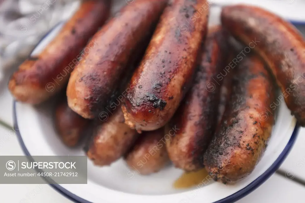 A tin plate stacked with cooked sausages on a table.